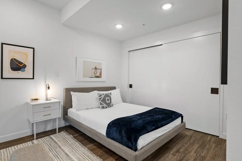 Área de dormitorio con una cama gris, una manta azul marino y almohadas blancas.