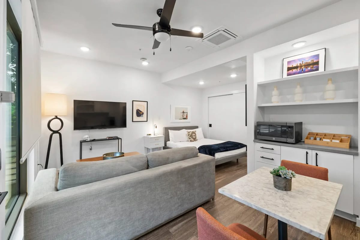 Apartamento tipo estudio moderno con cama, sofá, TV, cocina pequeña y comedor.