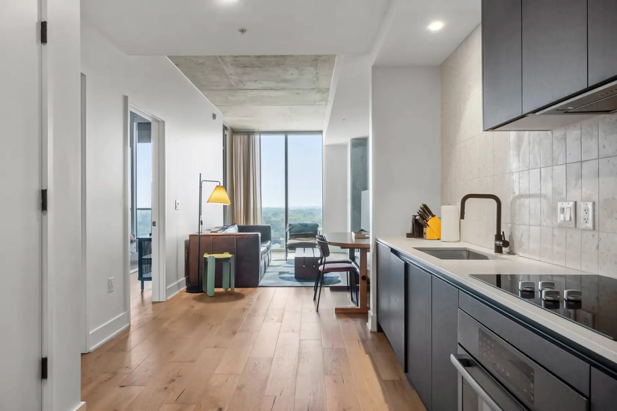 Modern apartment interior with a wooden floor, sleek kitchen, and bright living area with large windows.