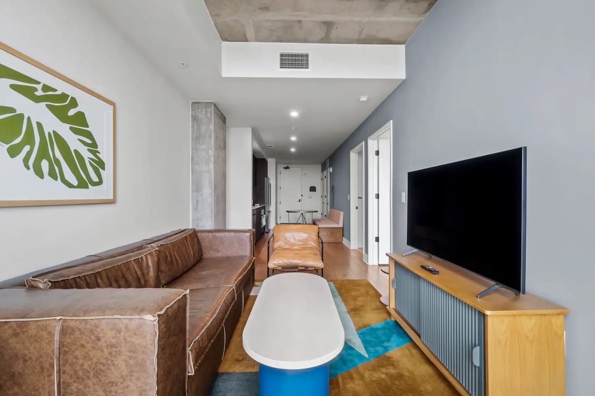Sala de estar moderna con sofá de cuero marrón, televisor, mueble de madera y una lámina de una hoja enmarcada.