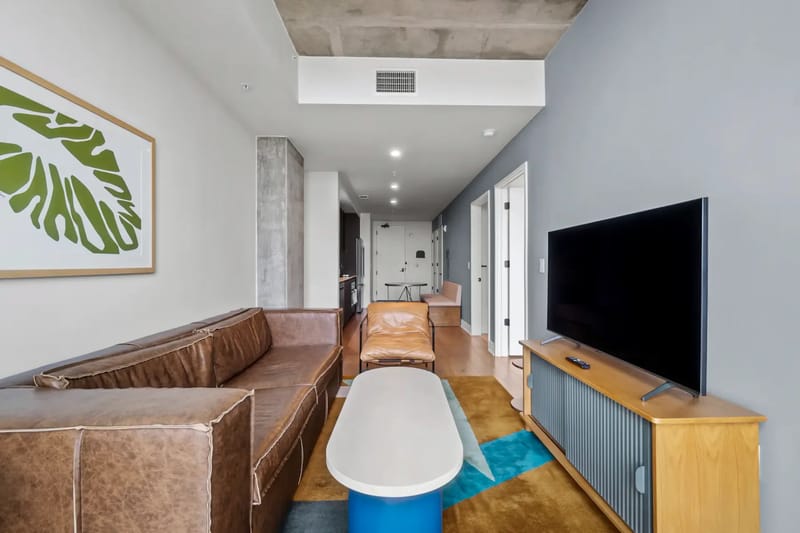 Sala de estar moderna con sofá de cuero marrón, televisor, mueble de madera y una lámina de una hoja enmarcada.