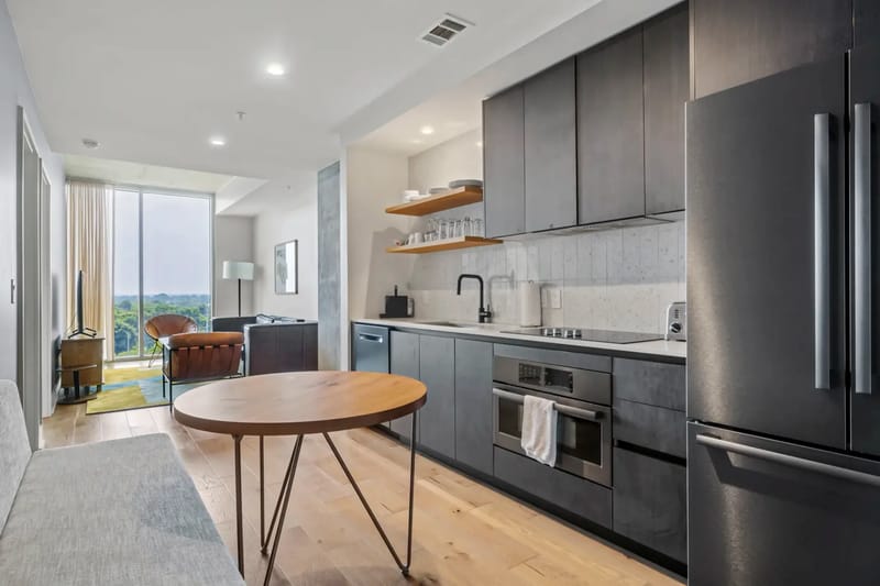 Cocina y sala de estar modernas de planta abierta con gabinetes oscuros, electrodomésticos de acero inoxidable y una ventana grande.