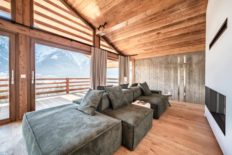 Amplio salón con grandes sofás mullidos, vigas de madera, una chimenea moderna y grandes ventanas.