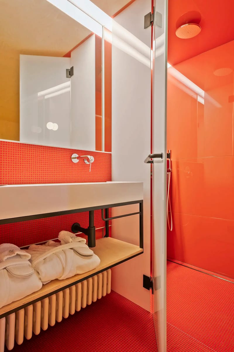Baño moderno con azulejos rojos, una puerta de ducha de cristal y un mueble de lavabo blanco.
