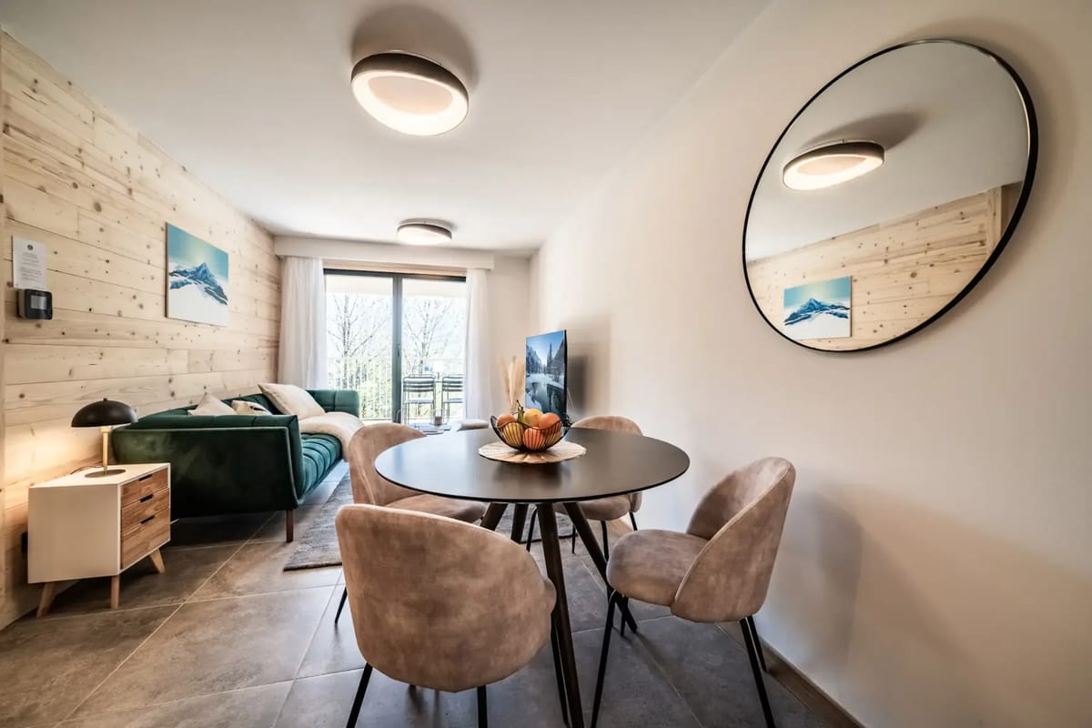 Modern open-plan kitchen and dining area with a round table, four upholstered chairs, and a minimalist black and wood kitchen.