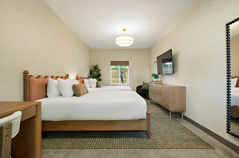 Two double beds, a large mirror, a wall-mounted TV, a wooden dresser, and a window with natural light.