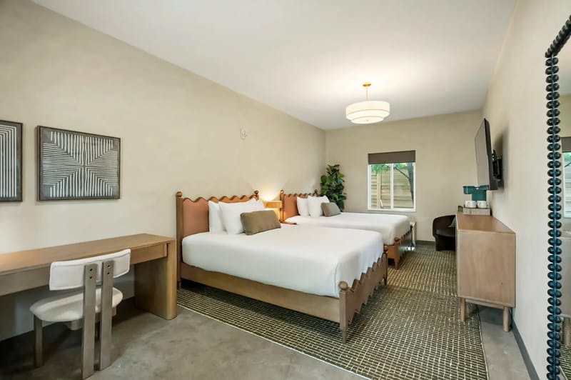 Two double beds, a desk with a chair, wall-mounted TV, and decor accents.