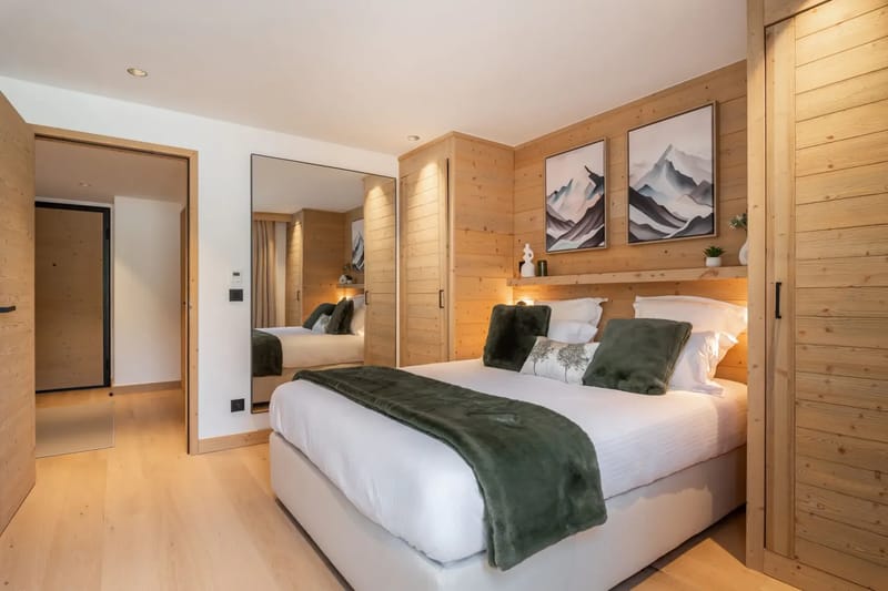Dormitorio acogedor con una cama grande, un televisor montado en la pared que muestra montañas, detalles de madera y una puerta de cristal que da a un balcón.