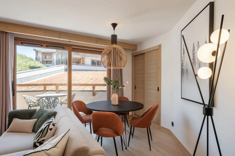 Salón moderno con un sofá beige, mesa de comedor redonda, sillas naranjas, una ventana grande, una lámpara decorativa y obras de arte minimalistas.