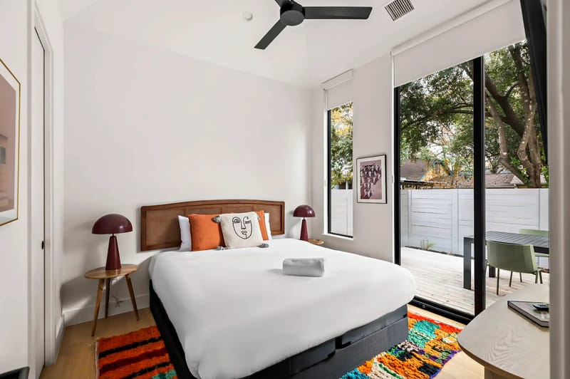 Bedroom with a large bed, colorful rug, side tables, and a large window opening toward a patio.