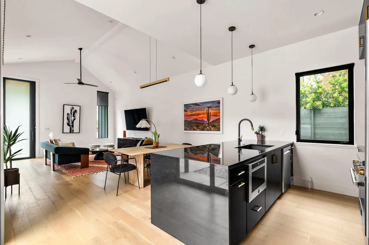 Open-plan living space with a kitchen island, dining table, seating area, pendant lights, and large windows.