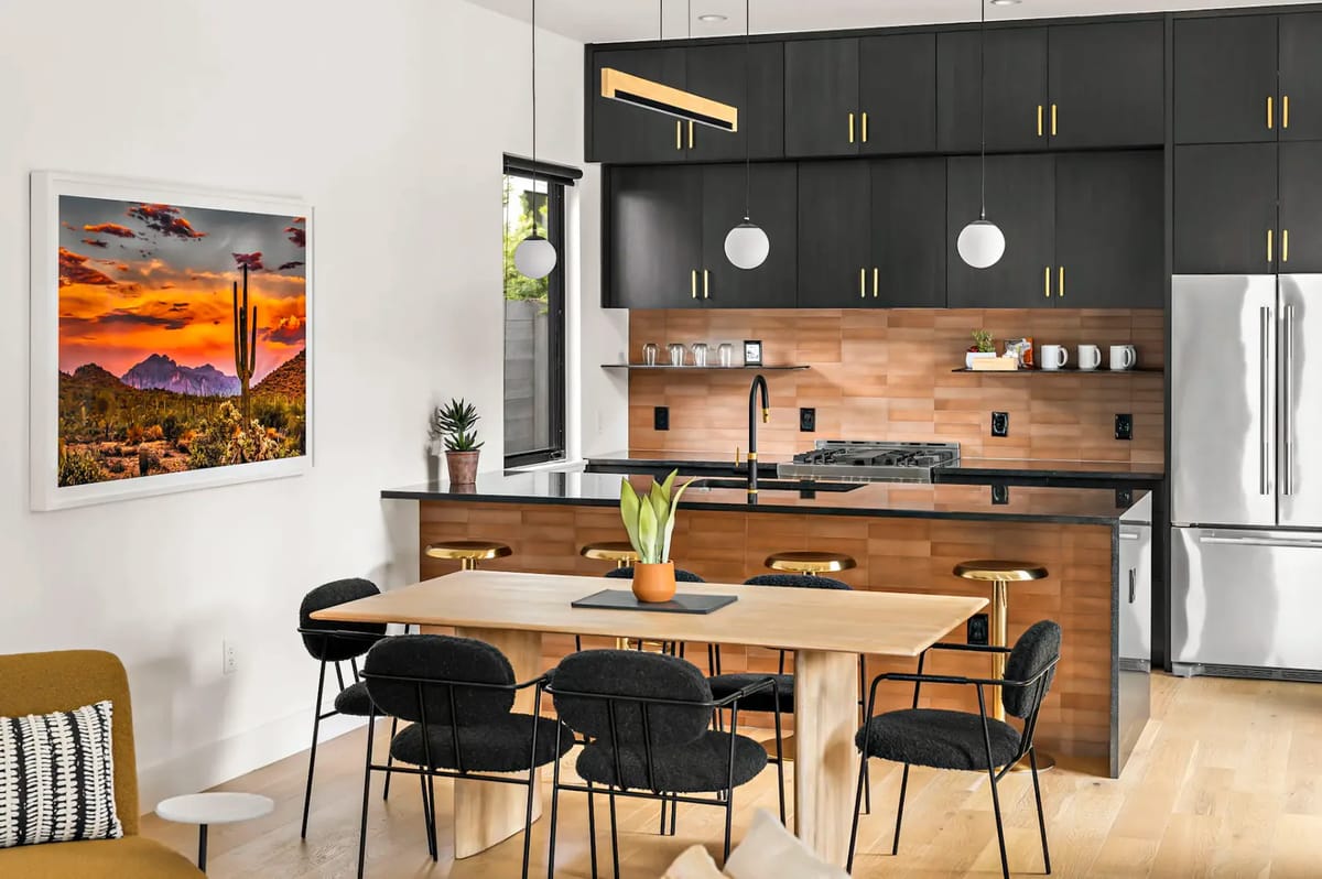 Modern kitchen and dining area with black cabinets, stainless-steel appliances, wooden flooring, and a landscape painting.