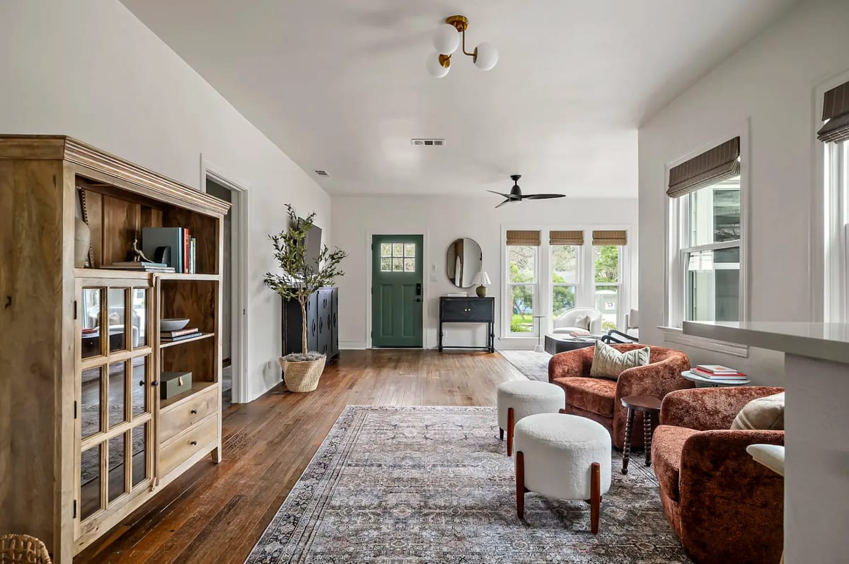Sala luminosa con pisos de madera, una alfombra vintage, dos sillones marrones, una estantería de madera y una planta en maceta.