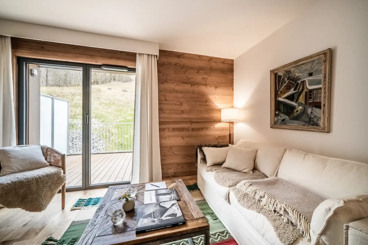 Cozy living room with a white sofa, colorful rugs, and a wall-mounted TV. A sliding door leads to an outdoor area.