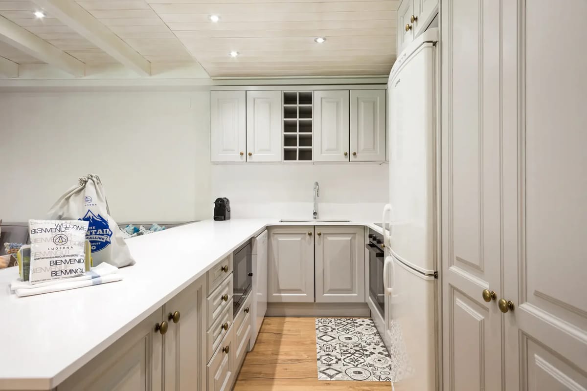 Cocina y zona de estar modernas de planta abierta con suelos de madera y vigas en el techo. La cocina cuenta con muebles de líneas depuradas y una gran isla, mientras que el salón tiene grandes ventanales y asientos acogedores.