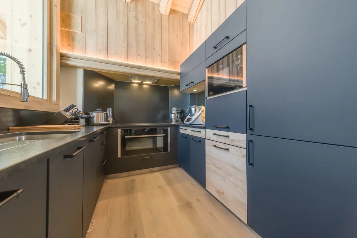 Cocina moderna con armarios azules, detalles de madera, electrodomésticos integrados y suelo de madera clara.