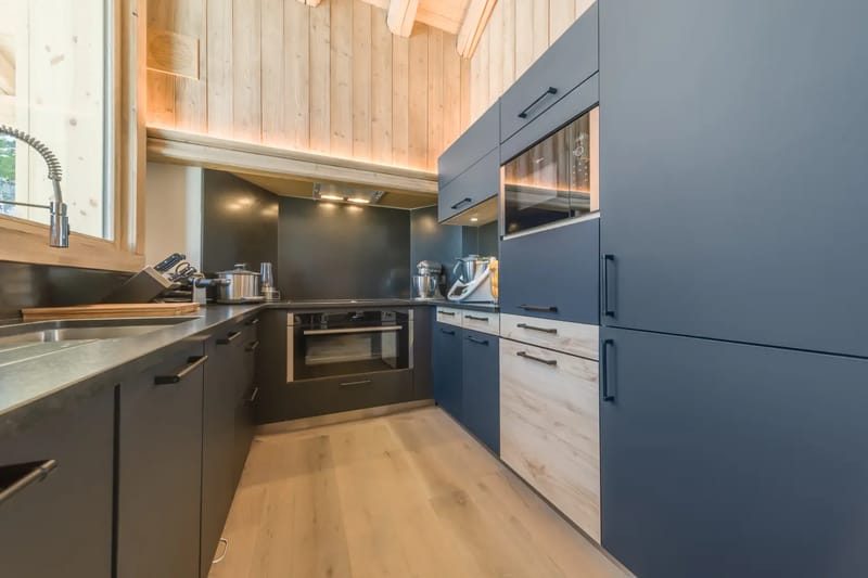 Modern kitchen with blue cabinets, wood accents, built-in appliances, and a light wooden floor.