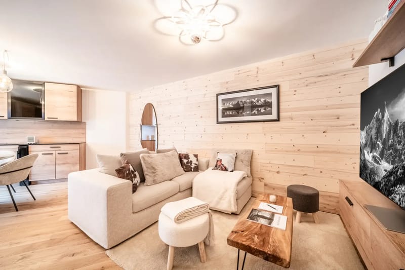 Living room with light wood paneling, a beige couch, wooden TV stand, large flat-screen TV, and a landscape photo on the wall.