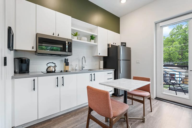 Cocina compacta con gabinetes blancos y encimera gris.