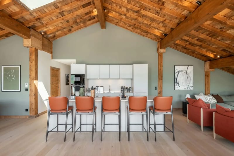 Amplio loft con vigas de madera, una ventana en el techo y cocina moderna; cuenta con taburetes de barra, mesa de comedor y zona de estar.