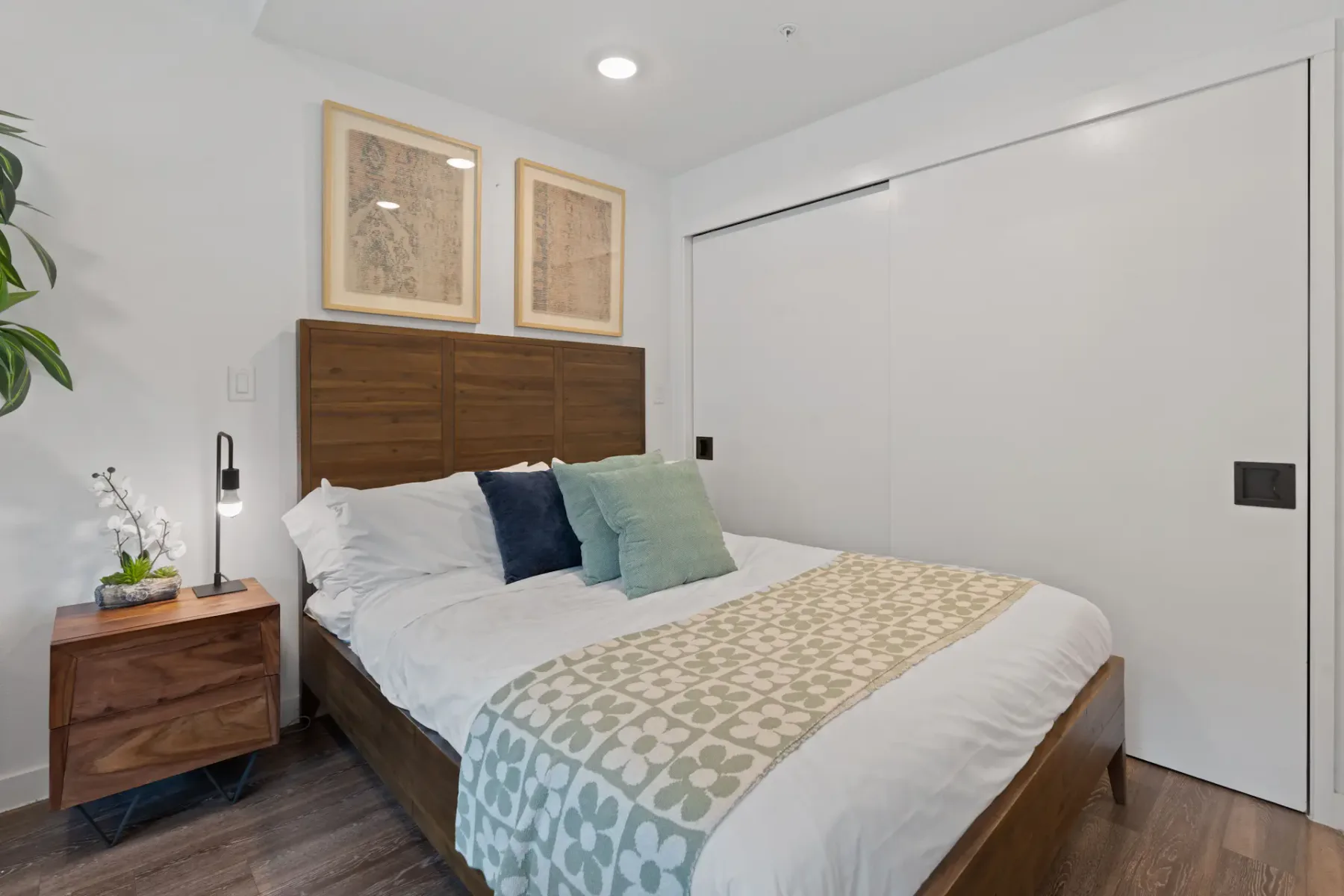 Bedroom area with a wooden bed, bedding, nightstand, and artwork.