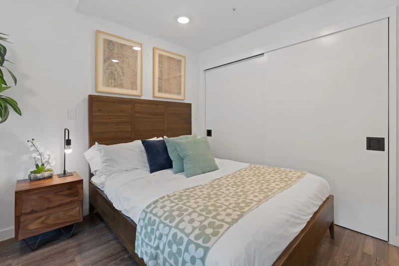 Bedroom area with a wooden bed, bedding, nightstand, and artwork.