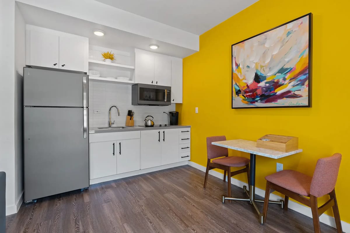 Modern kitchenette with white cabinets, stainless steel appliances, and a small dining table.