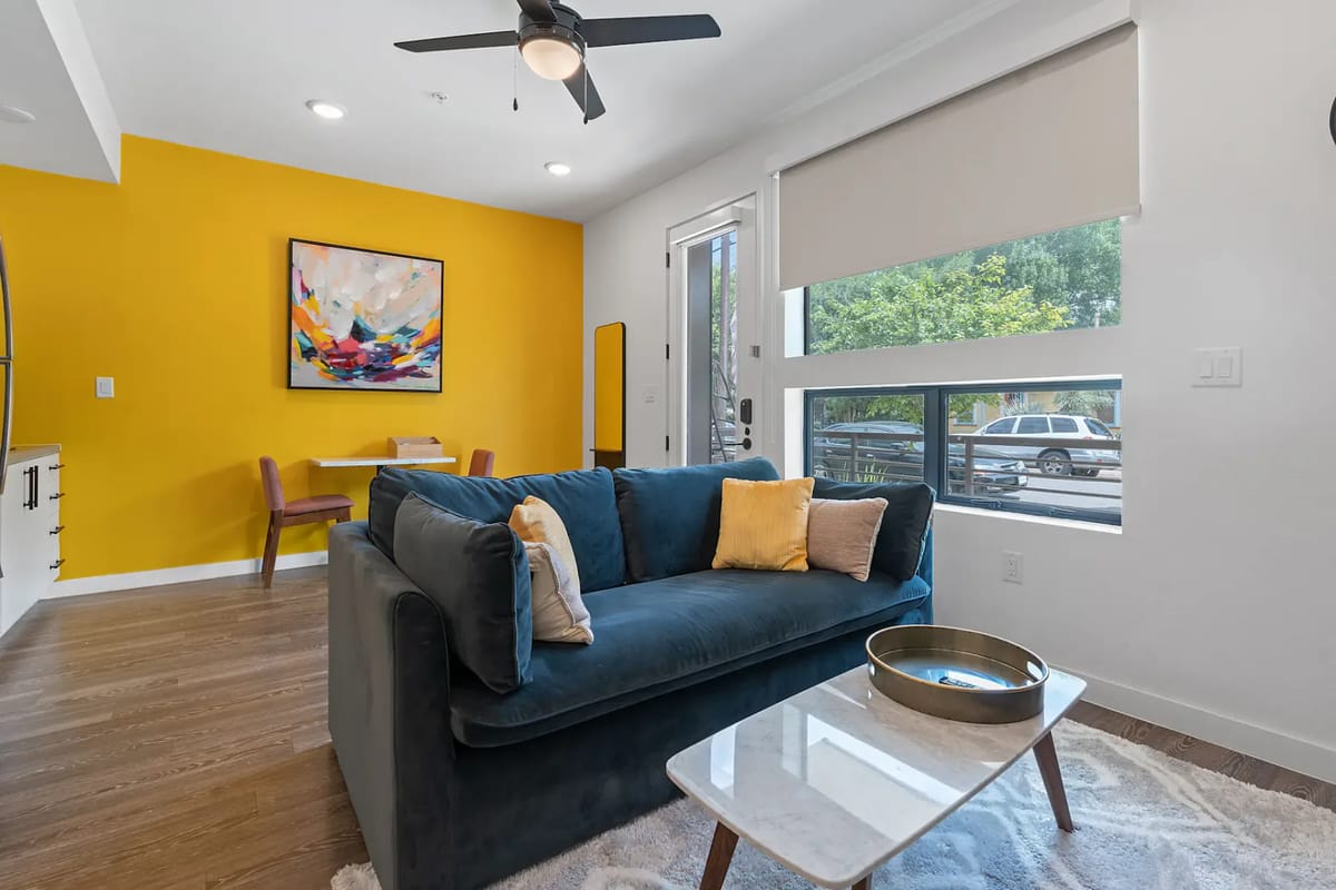 Modern living room with a blue sofa, TV, large window, and adjacent bed area.