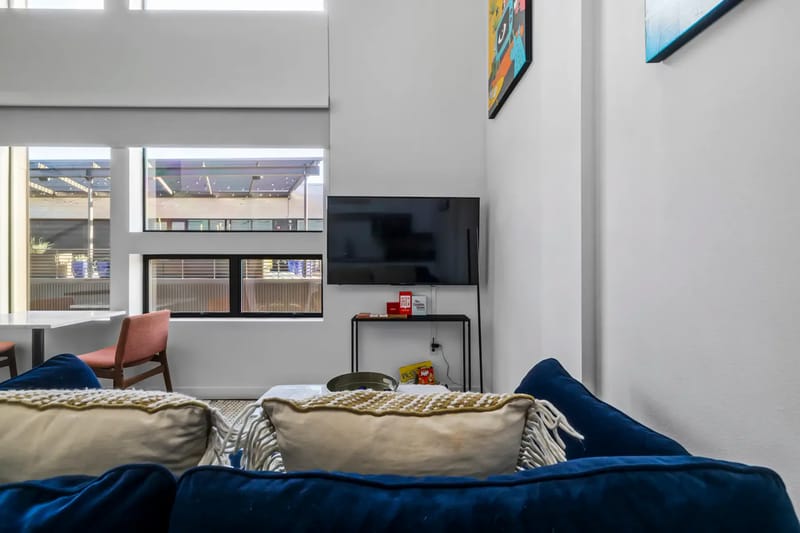 Cozy living room with two blue sofas, a wall-mounted TV, artwork, and a small dining area.