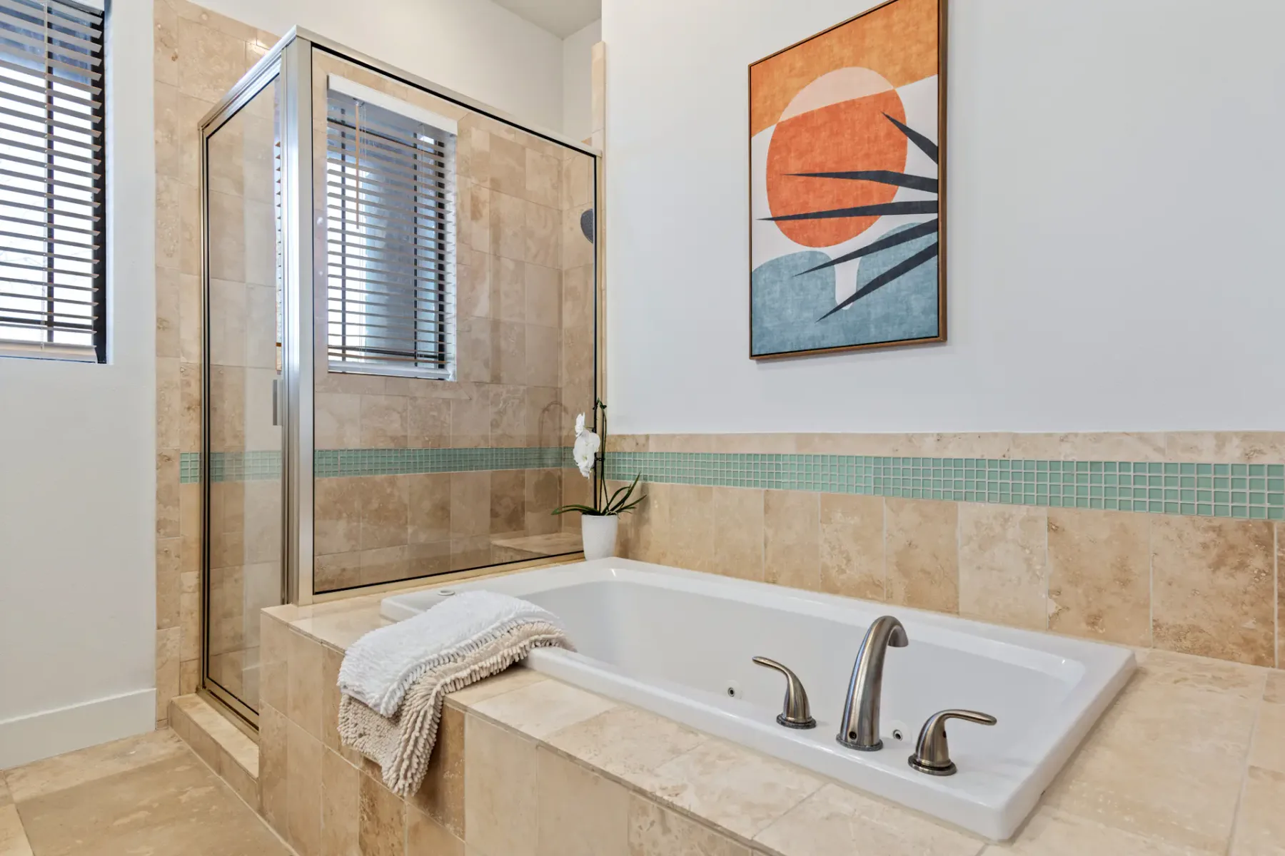 Baño moderno con una bañera revestida de azulejos, una ducha cercana, arte decorativo en la pared y una planta pequeña. Hay una toalla sobre el borde de la bañera.