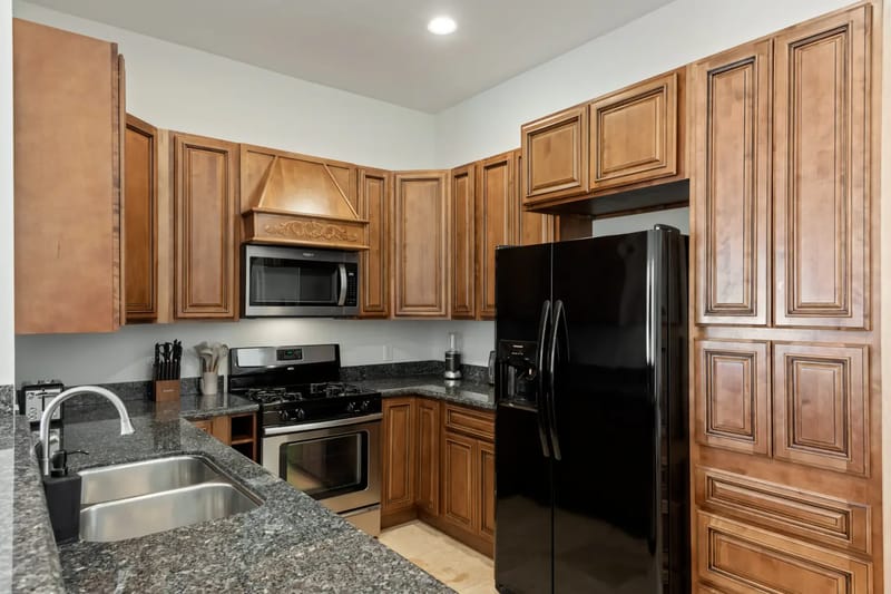 Modern kitchen with wooden cabinets, black granite countertops, stainless steel appliances, black fridge, and a double sink.
