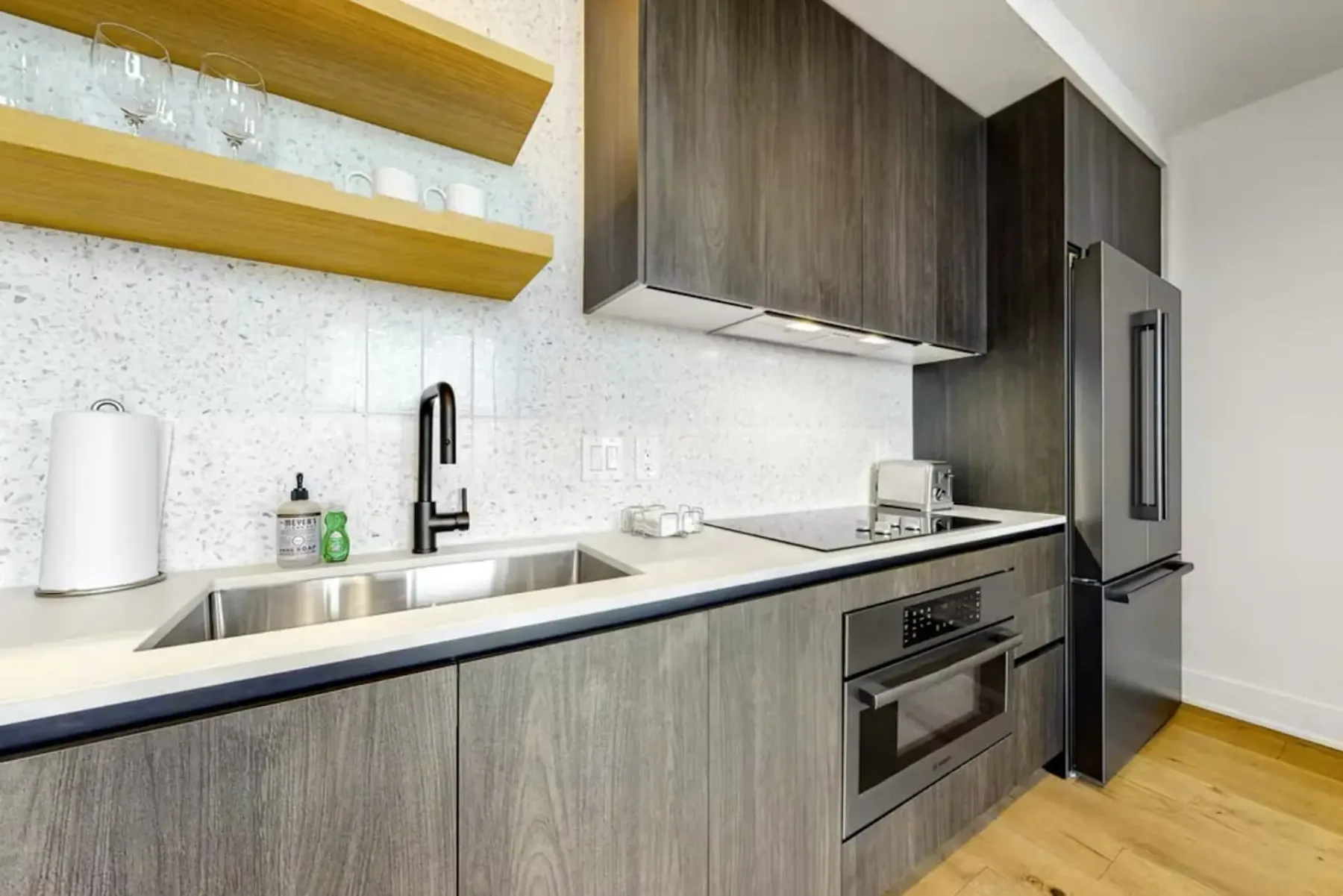Modern kitchen with wood cabinetry, stainless steel sink, electric stove, oven, toaster, and marble backsplash.