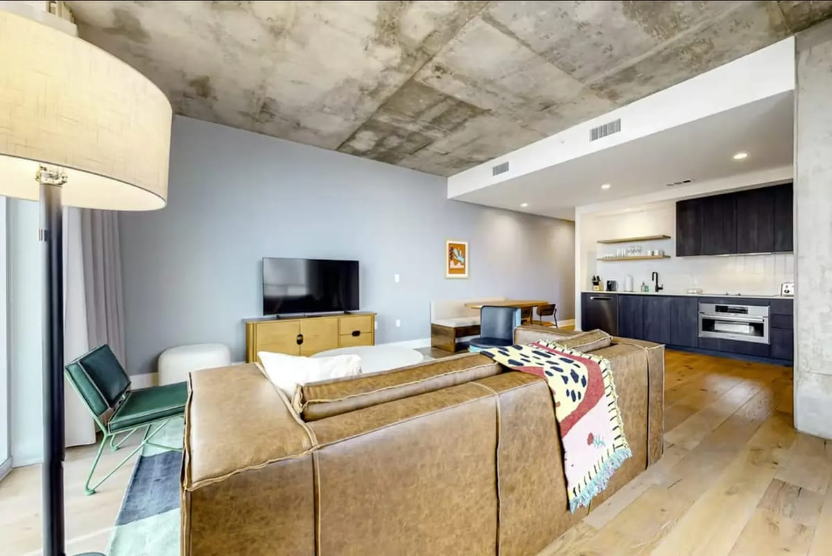 Modern open-concept living room with a sofa, flat-screen TV, and kitchen.
