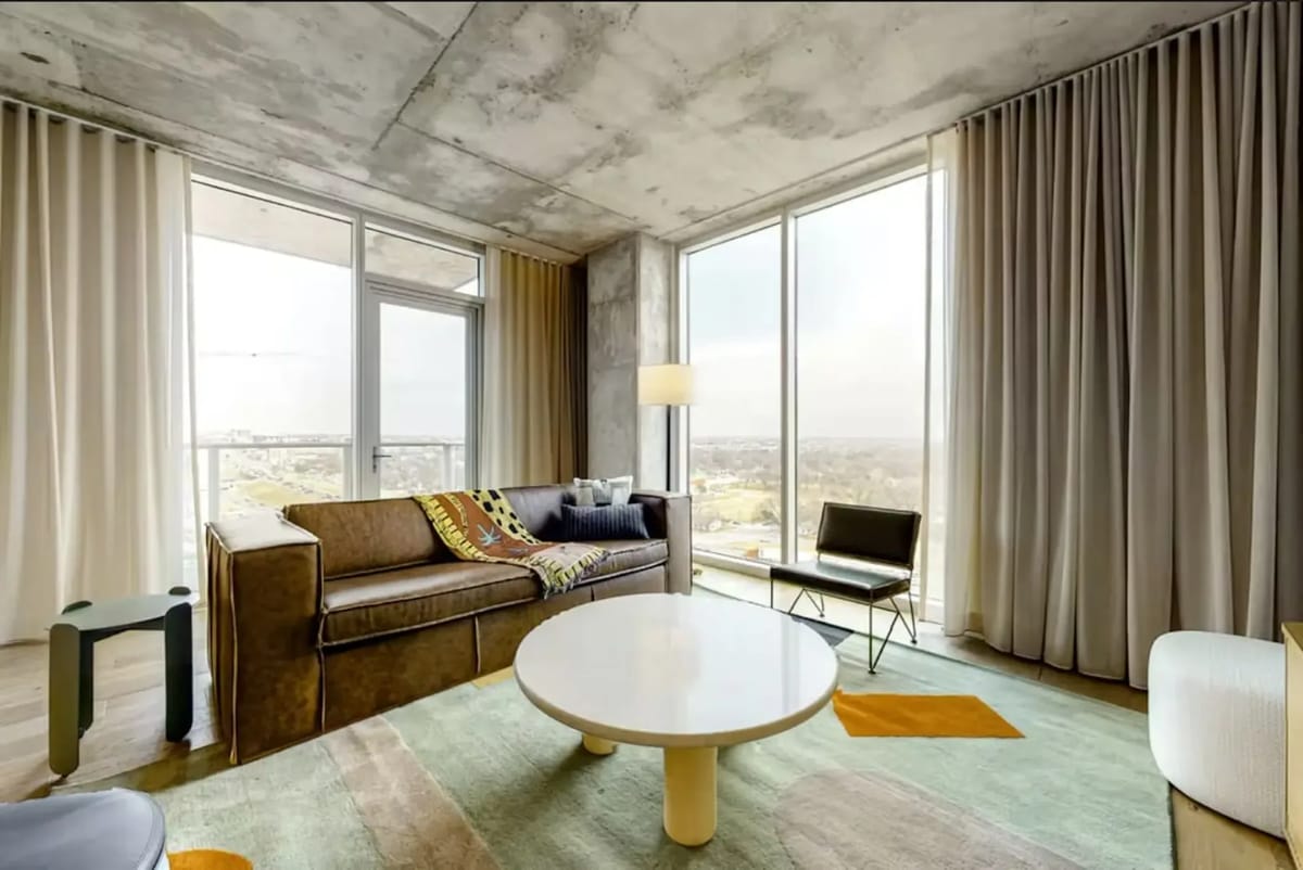 Modern living room with a brown sofa, circular coffee table, floor-to-ceiling windows, and a cityscape view.
