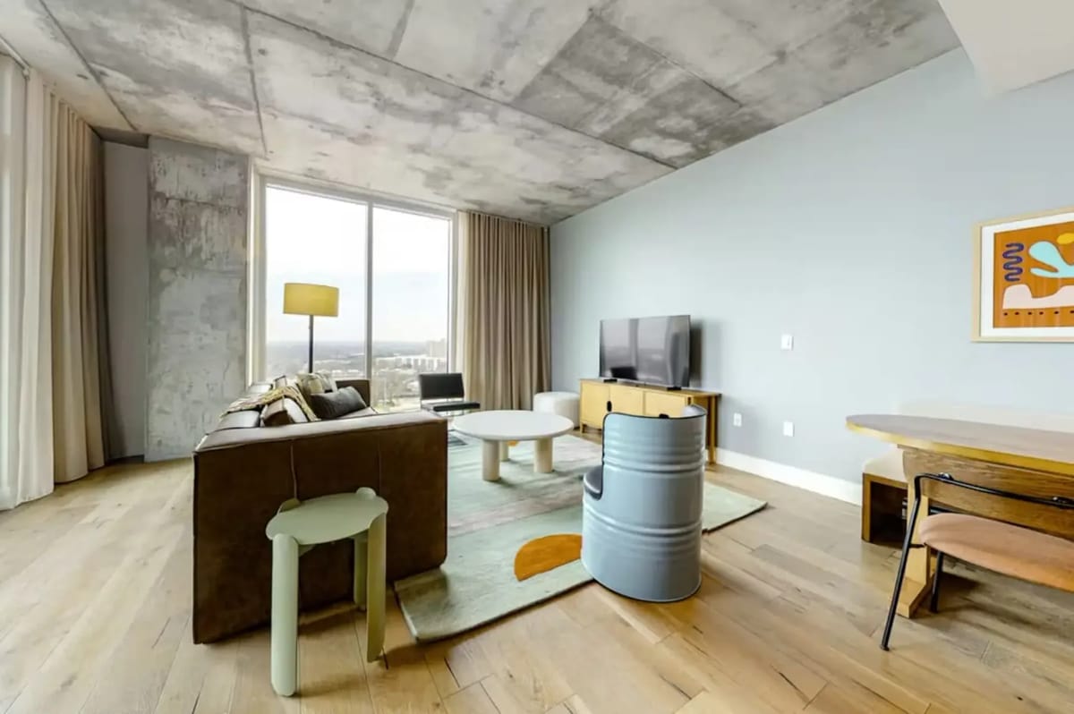 Modern living room with a brown couch, colorful rug, round tables, and a flat-screen TV.