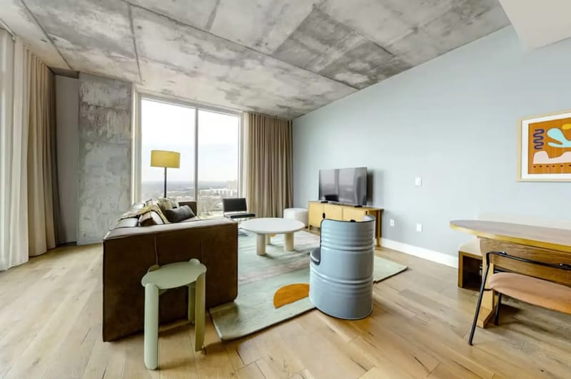 Sala de estar moderna con un sofá marrón, una alfombra colorida, mesas redondas y un televisor de pantalla plana.
