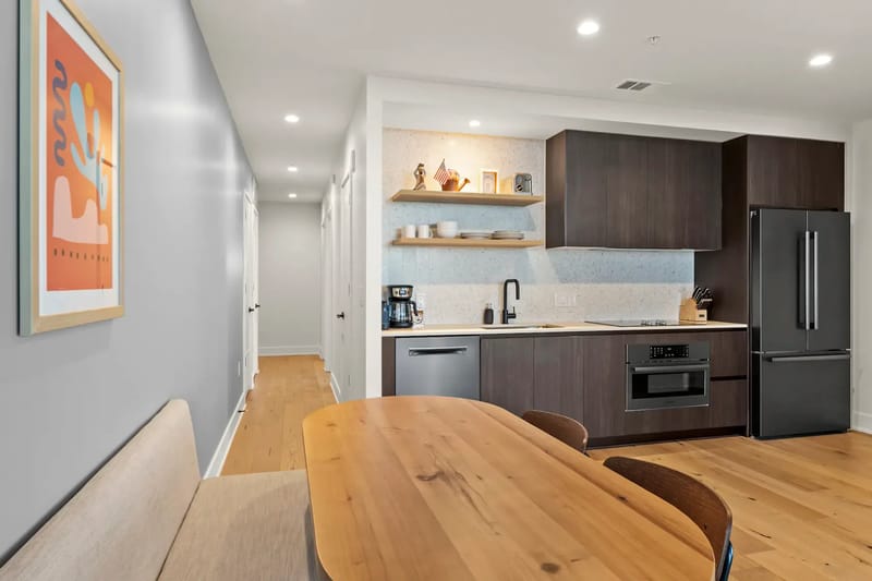 Cocina moderna con gabinetes de madera oscura, electrodomésticos de acero inoxidable y una mesa de comedor de madera.