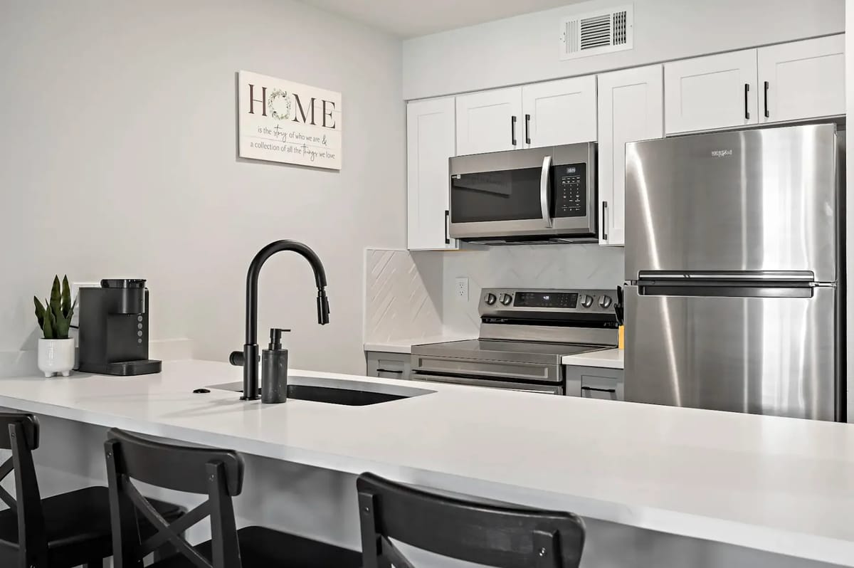 Cocina moderna con electrodomésticos de acero inoxidable, gabinetes blancos, un grifo negro y una encimera blanca.