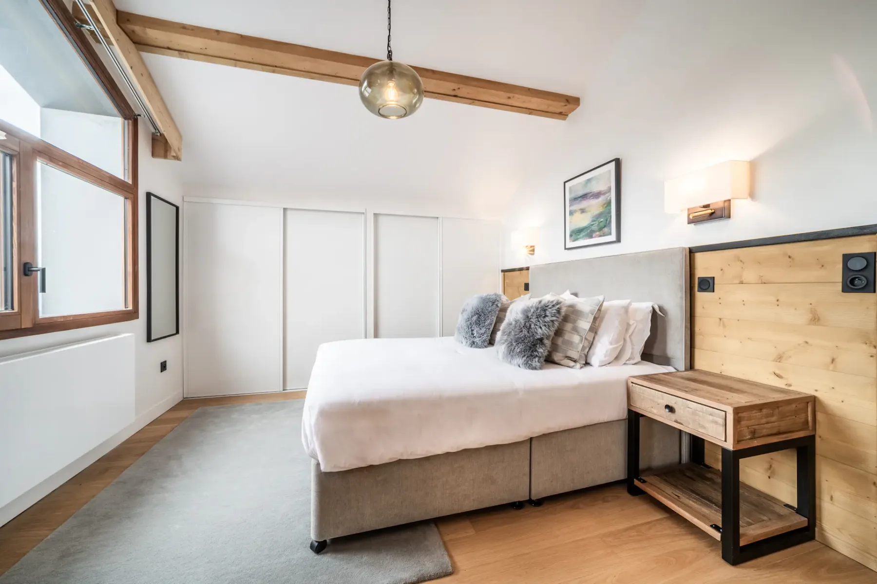 Un dormitorio acogedor y bien iluminado con una cama doble, detalles de madera y lámparas modernas.