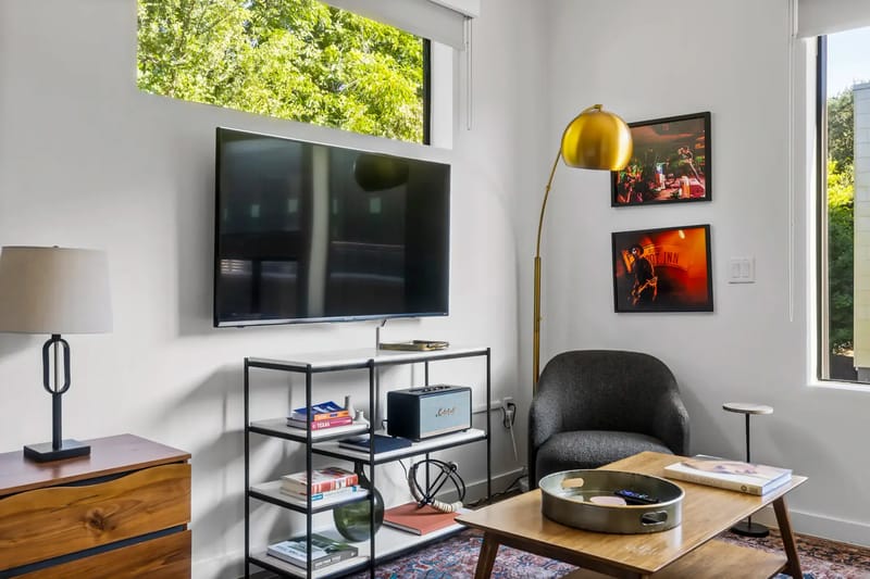 Sala de estar con un televisor, una estantería, una silla negra, una lámpara de pie dorada y obras de arte en la pared.