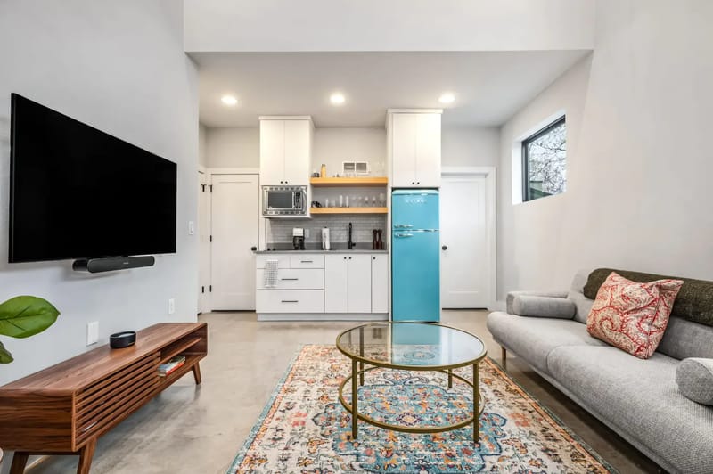 Sala de estar elegante con un televisor montado en la pared, obras de arte y una consola. Se ven una lavadora y una secadora en la habitación contigua.