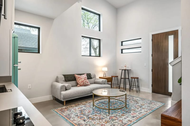 Sala de estar moderna con pisos de madera, decoración ecléctica, ventiladores de techo y ventanas luminosas. Cuenta con una zona para sentarse, un comedor abierto y obras de arte expuestas.
