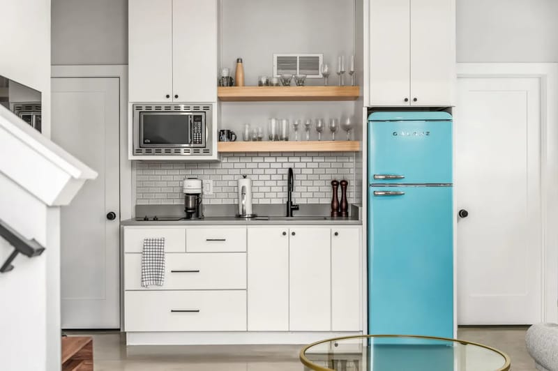 Una cocina luminosa con gabinetes blancos, encimeras de azulejos azules, un horno doble y vista hacia un comedor.