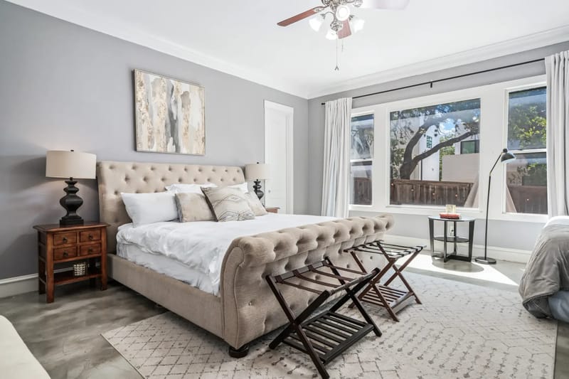 Modern bedroom with a tufted bed, neutral tones, large windows, wooden side tables, and benches.