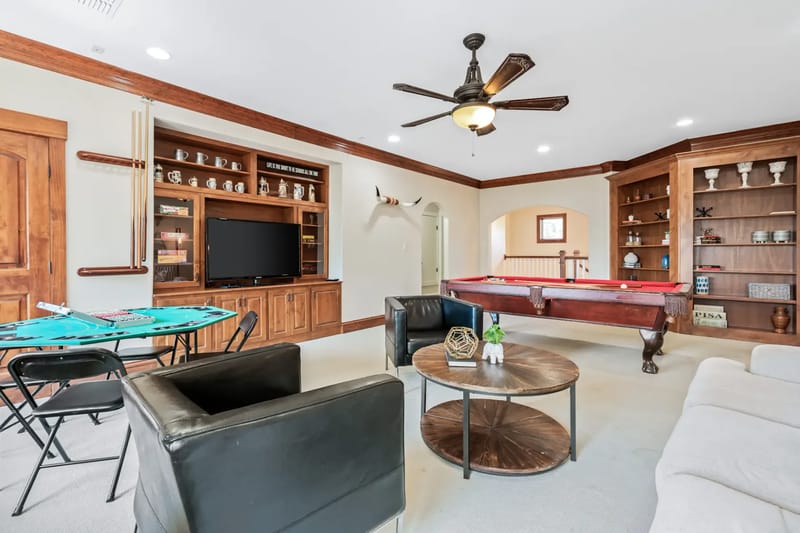 Spacious game room with a pool table, poker table, TV, leather chairs, and wooden shelves.