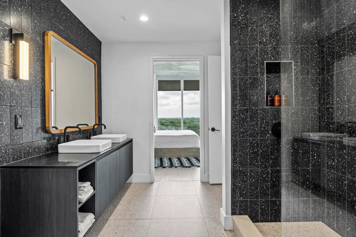 Baño moderno con mueble de lavabo negro, dos lavabos, espejo grande y ducha con cerramiento de vidrio.