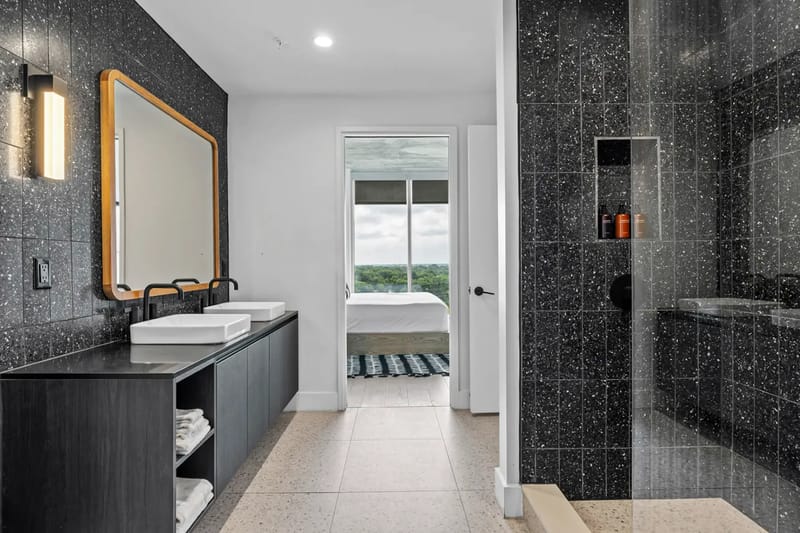 Baño moderno con mueble de lavabo negro, dos lavabos, espejo grande y ducha con cerramiento de vidrio.