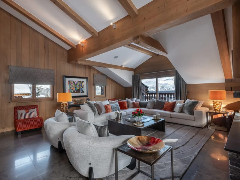 Cozy living room with wooden beams, large sofas, colorful cushions, modern art, and a mountain view through large windows.