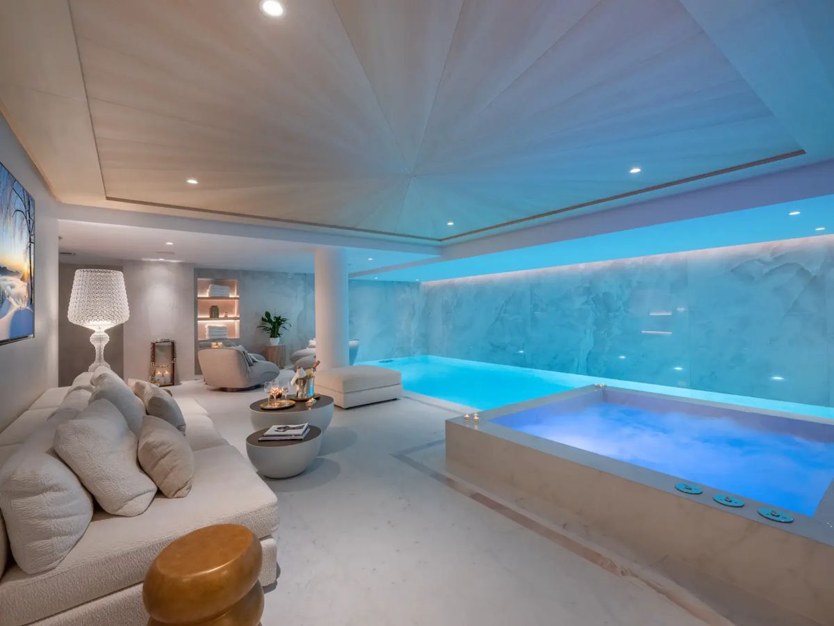 Lujoso spa interior con una piscina cubierta iluminada, una bañera de hidromasaje, asientos mullidos e iluminación tenue.