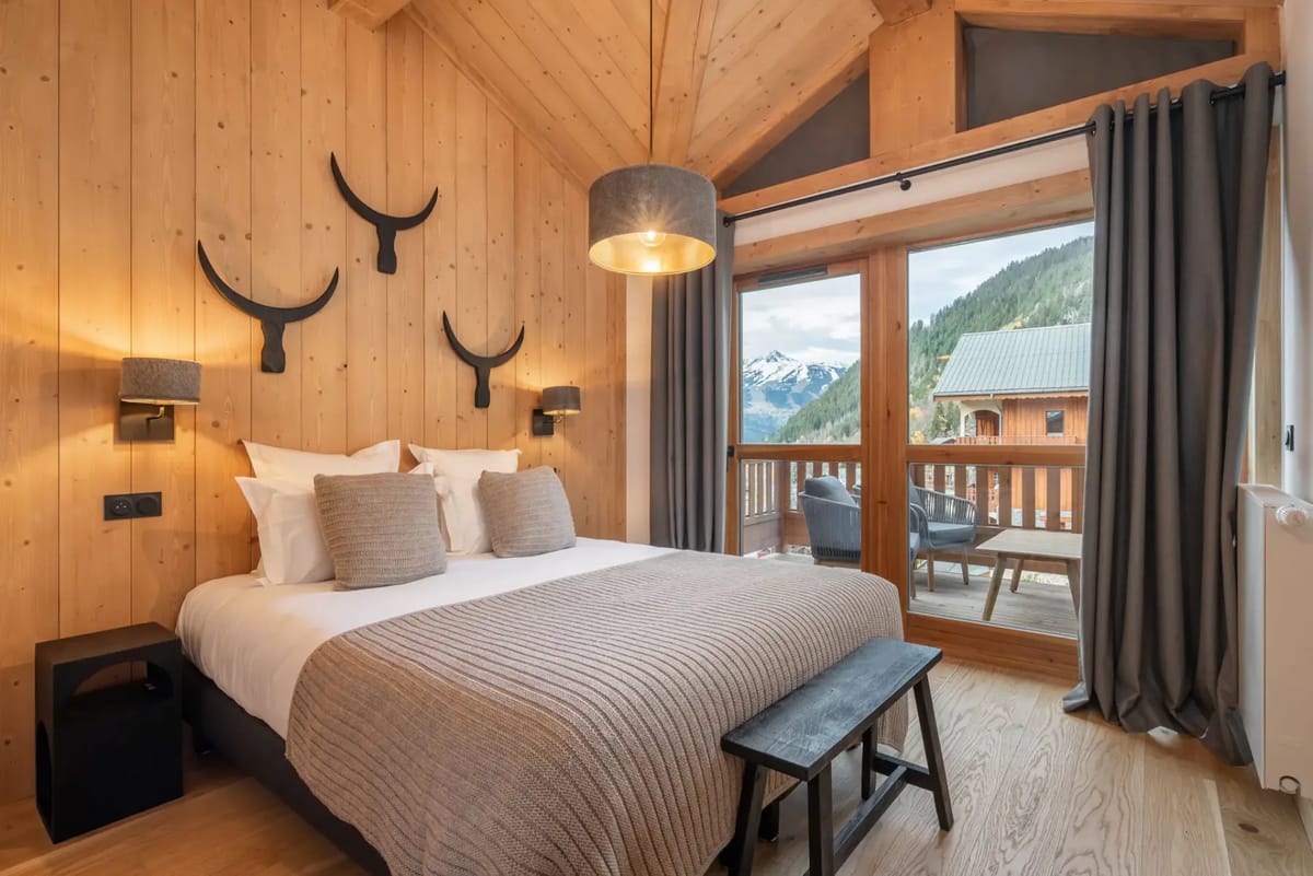 Cozy bedroom with wooden walls, a double bed, decorative antlers, and a balcony view of mountains.
